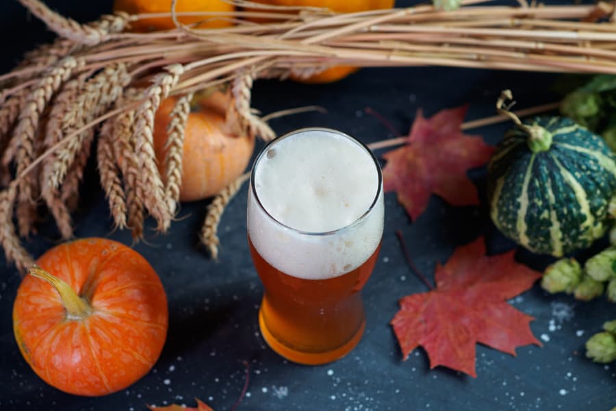 Glass of beer on table surrounded by pumpkins, leaves, and squash